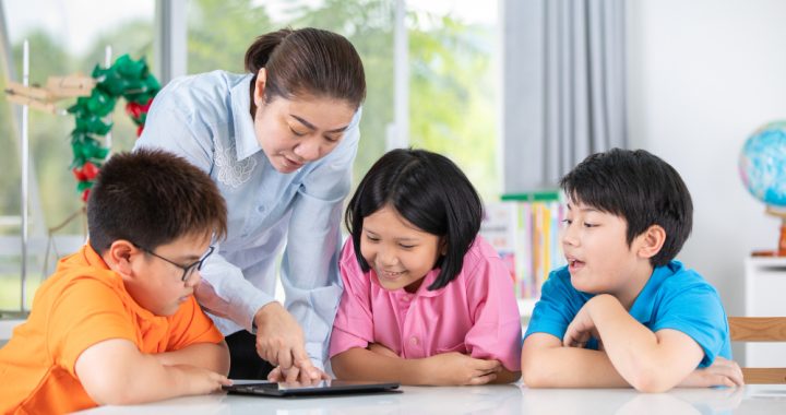 Guru mendampingi murid menggunakan tablet digital di kelas